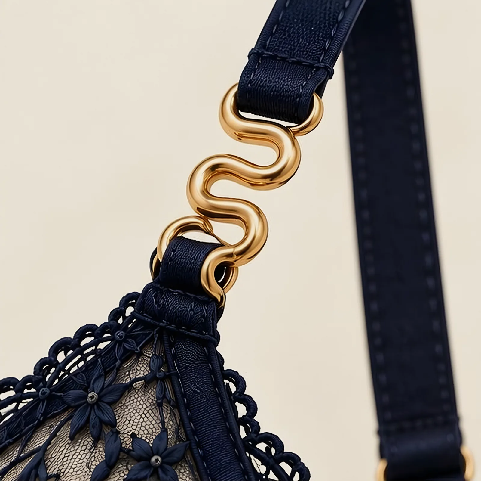 A gold serpent clasp joining a midnight satin strap to an embroidered lace cup.
